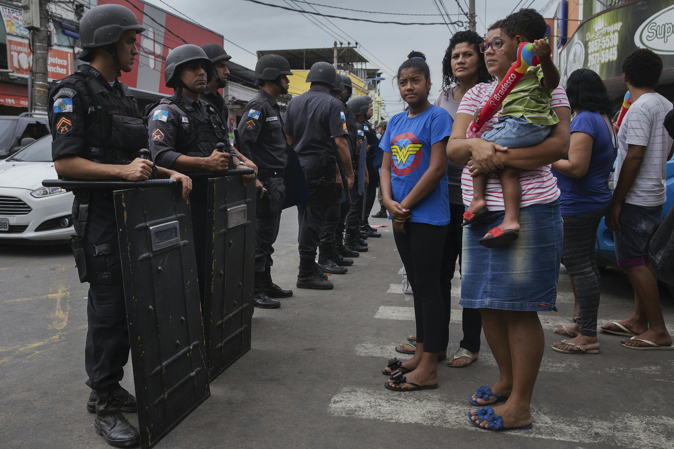 Military police and residents along the Summer Olympic’s torch relay route in the Duque de Caxias city of Rio de Janeiro state, Aug. 3, 2016. With a president facing impeachment and a recession stunting the national economy, nearly two-thirds of Brazilians believe that hosting the Summer Games will have a negative effect on the country. (Lalo de Almeida/The New York Times)