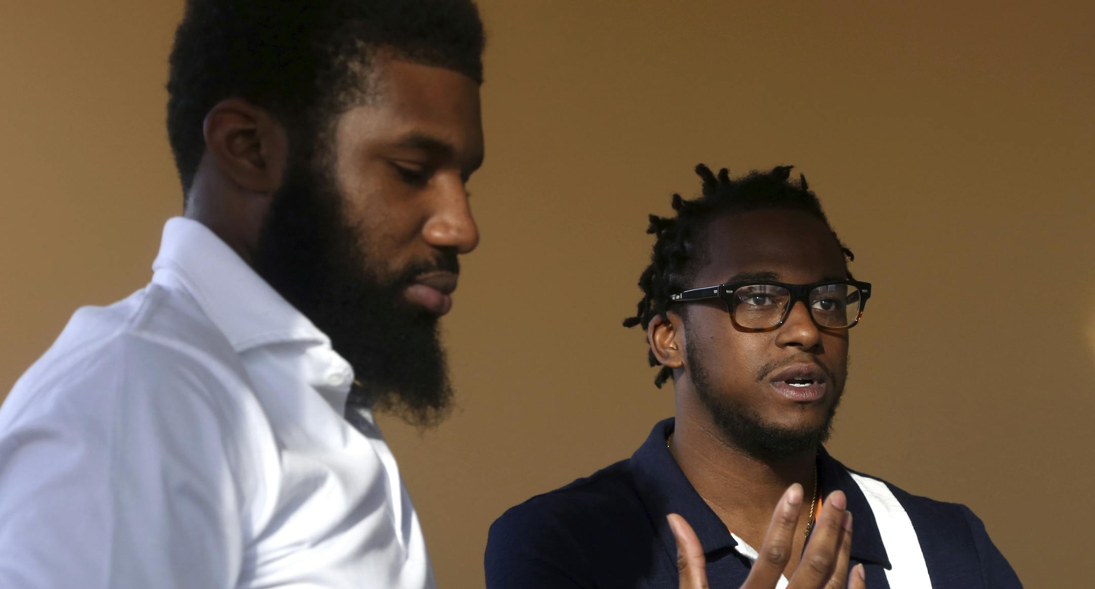 In this Wednesday, April 18, 2018 photo, Rashon Nelson, left, listens as and Donte Robinson, right, addresses a reporter's question during an interview with The Associated Press in Philadelphia. Their arrests at a local Starbucks quickly became a viral video and galvanized people around the country who saw the incident as modern-day racism. In the week since, Nelson and Robinson have met with Starbucks CEO Kevin Johnson and are pushing for lasting changes to ensure that what happened to them doe
