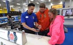 FILE - In this Friday, Nov. 27, 2015, file photo, Best Buy mobile associate Jonathan Maust, left, shows a smartphone to customers Brad Oaks and his wi