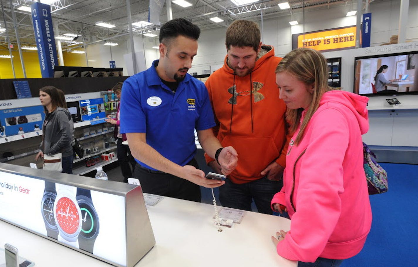 FILE - In this Friday, Nov. 27, 2015, file photo, Best Buy mobile associate Jonathan Maust, left, shows a smartphone to customers Brad Oaks and his wife, Nicole, of South Fork, Pa., in Johnstown, Pa. American businesses stepped up hiring in November, led by strong gains in retail, finance and other service industries, payroll processor ADP reported, Wednesday, Dec. 2, 2015. (John Rucosky/The Tribune-Democrat via AP, File)