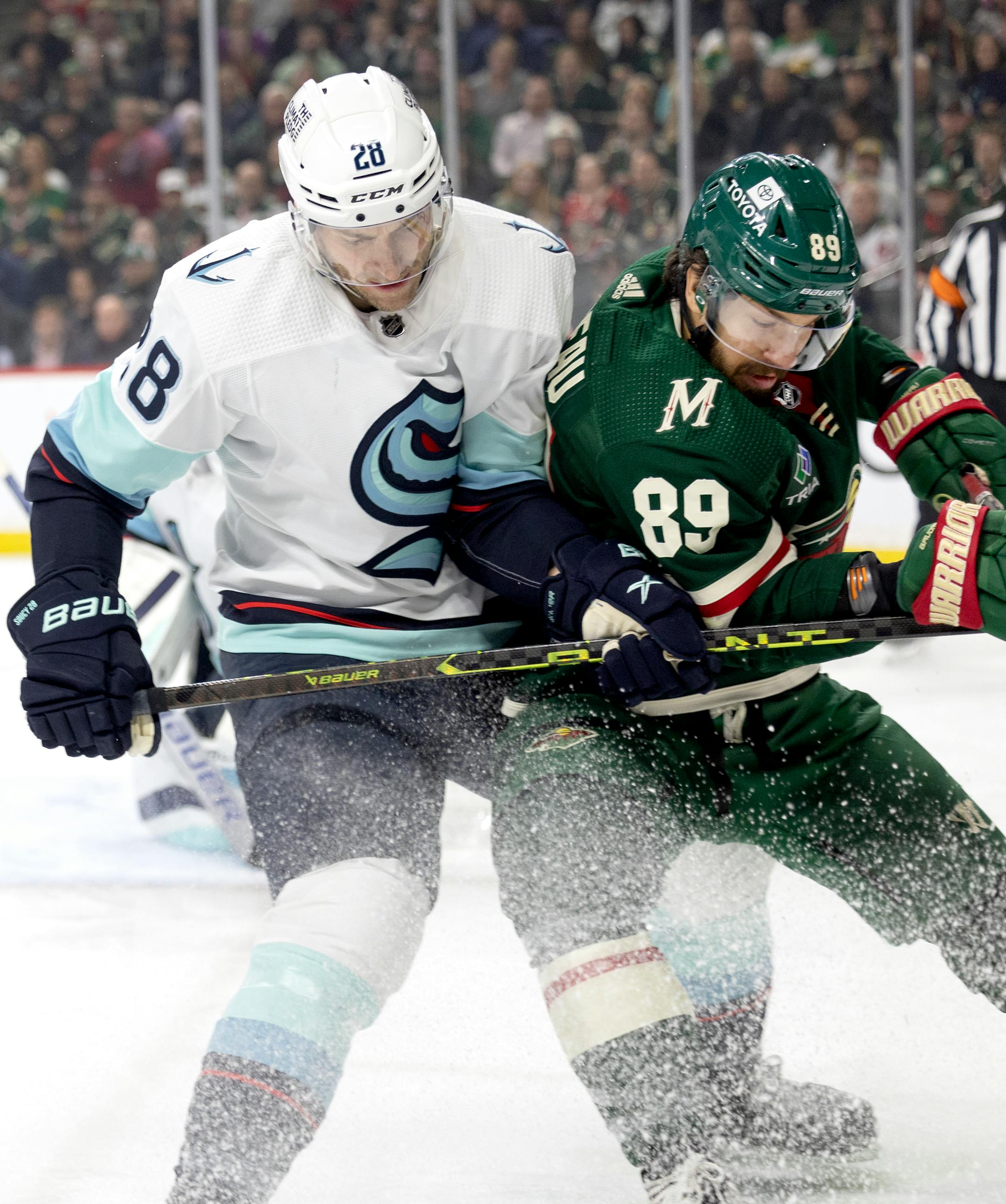 Carson Soucy (28) of the Seattle Kraken and Frederick Gaudreau (89) of the Minnesota Wild battle for the puck in the first period.