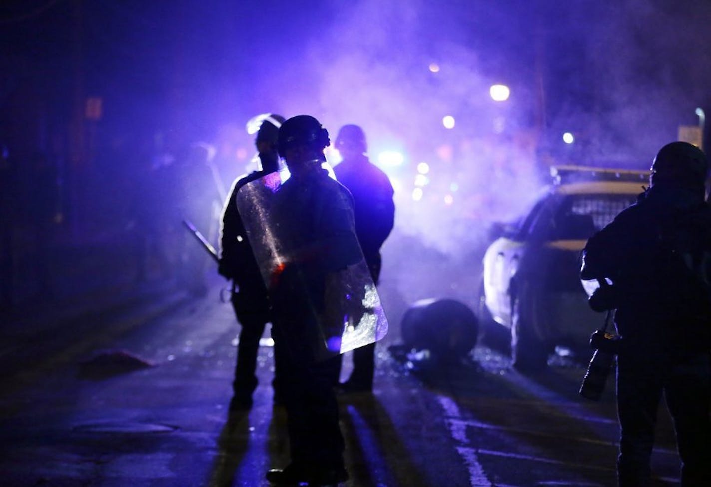 FILE - In this Nov. 25, 2014 file photo, police officers watch protesters as smoke fills the streets in Ferguson, Mo. The fatal police shooting of 18-year-old Michael Brown put Ferguson in the national spotlight. Amid a national push for greater police accountability, voters in several major cities have approved measures to create or strengthen civilian oversight of local law enforcement. The trend reflects growing public demand for independent reviews of misconduct after deadly police encounter