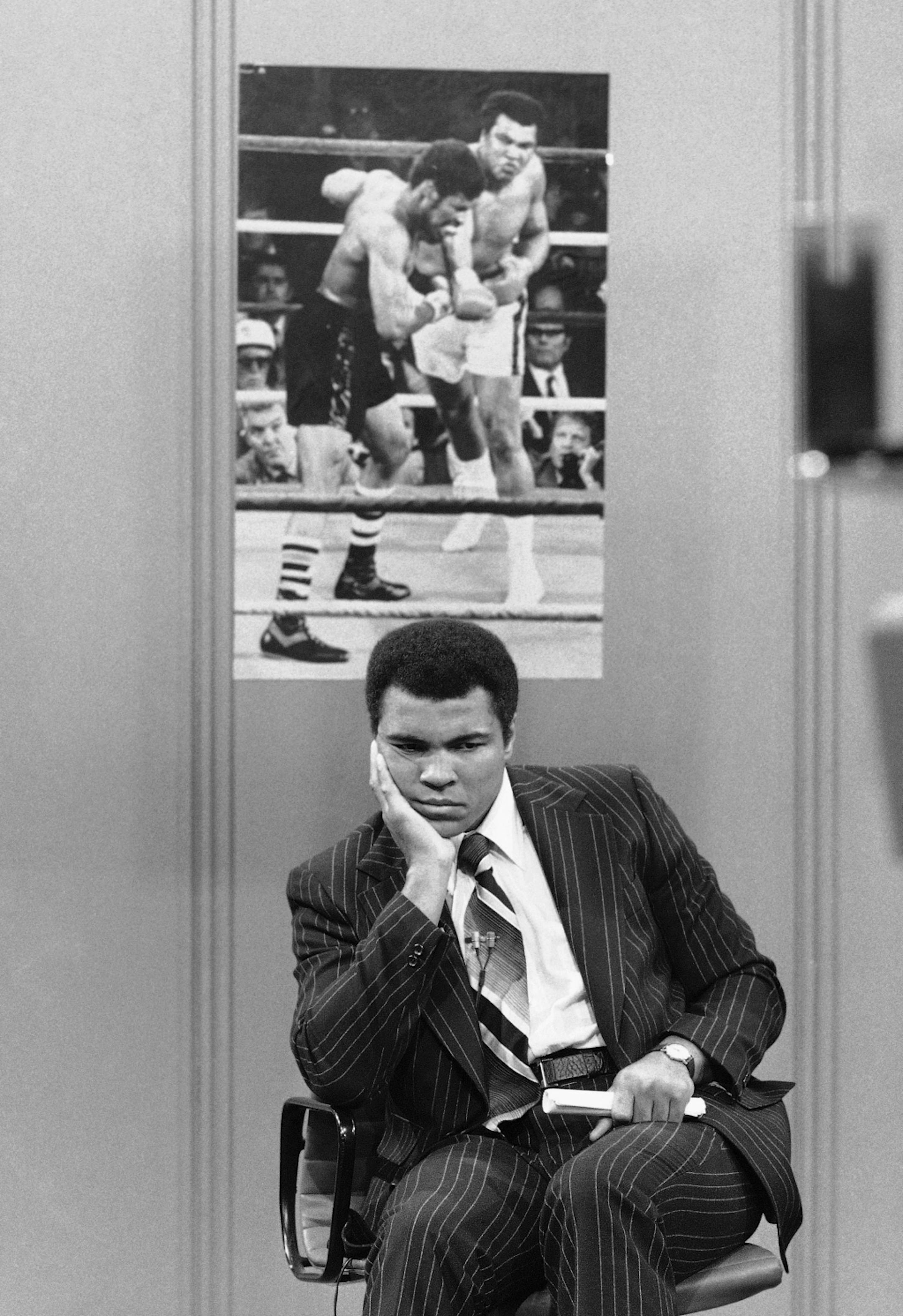 Former heavyweight champion Muhammad Ali on Saturday, March 4, 1978, sits beneath a photo of himself in action against current title holder Leon Spinks. Ali was appearing on a program televised by CBS in New York. He said he should be allowed to fight Spinks in a bid to gain the heavyweight title for the third time. (AP Photo/Ray Stubblebine) ORG XMIT: APHS285329
