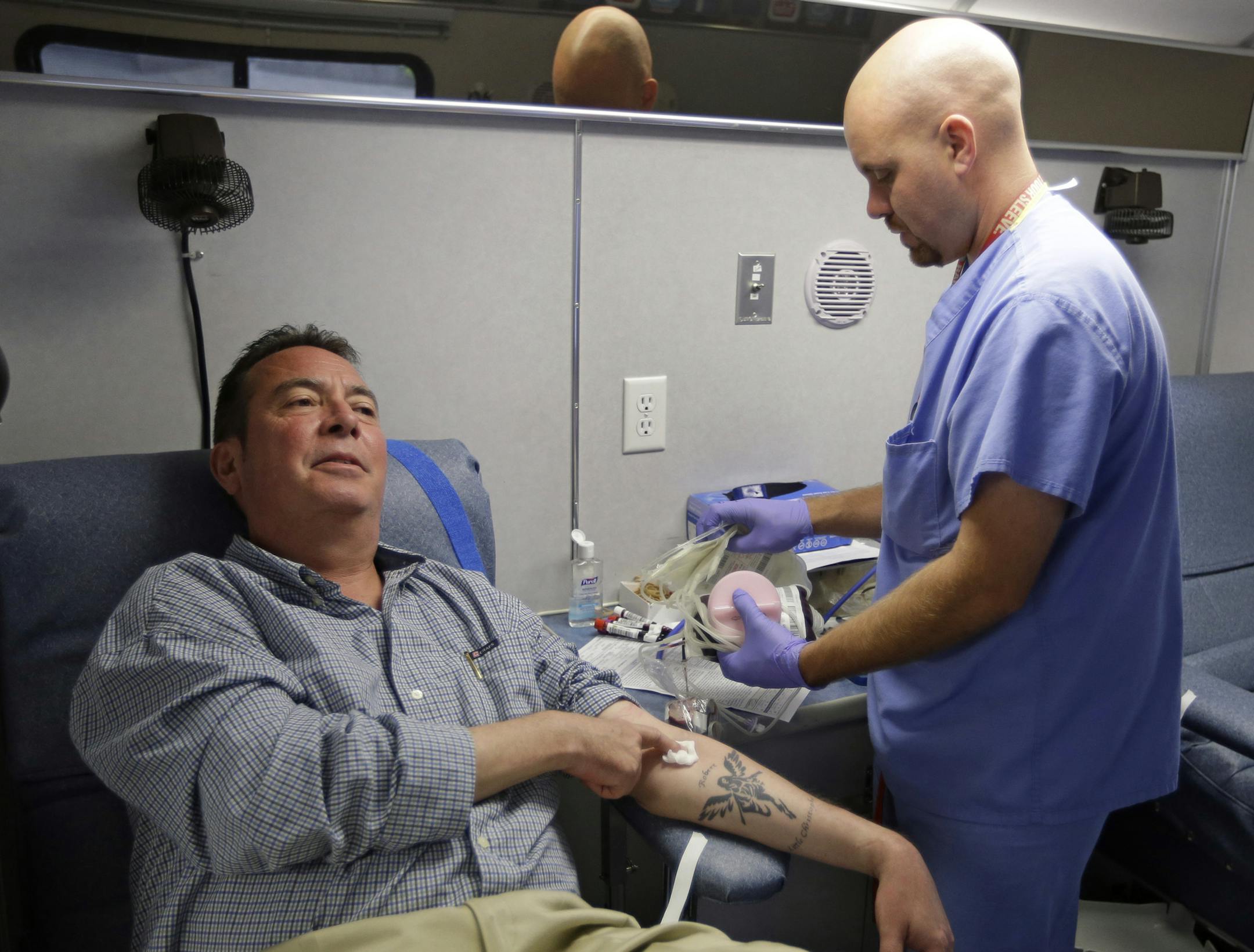 In this Aug. 20, 2013, photo, technician Greg Snyder, right, finishes up a blood draw from Chris Page after he donated blood in an Indiana Blood Center Bloodmobile in Indianapolis. The Indiana Blood Center announced in June 2013 that it would reduce its mobile operations, close a donor center and cutting other costs because demand from hospitals had fallen 24 percent from the previous year. This is largely due to fewer elective surgeries and medical advances that curb bleeding in the operating r