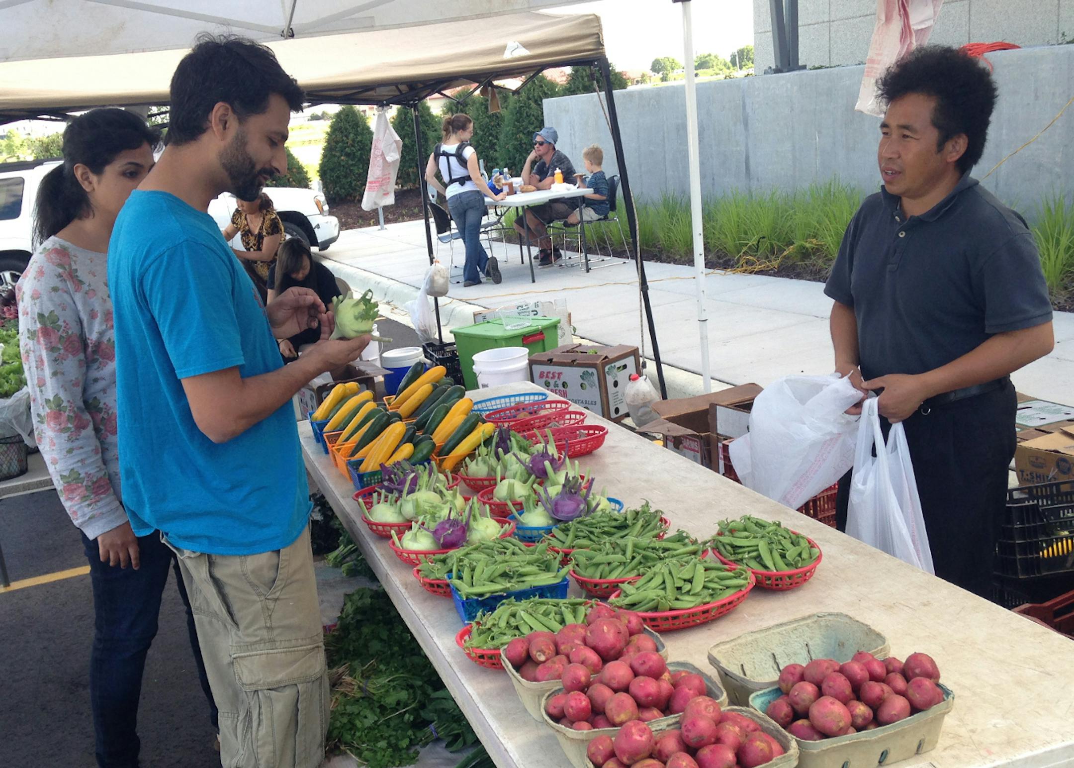 Farhan Sohail, a student at the University of Minnesota, buys vegetables at the weekly farmers market at The Good Acre in Falcon Heights. Naton Vang of St. Paul, right, grows these vegetables at his farm in Rosemount.