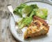 A slice of goat cheese, green onion and potato tart served with salad greens.