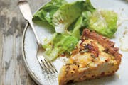 A slice of goat cheese, green onion and potato tart served with salad greens.