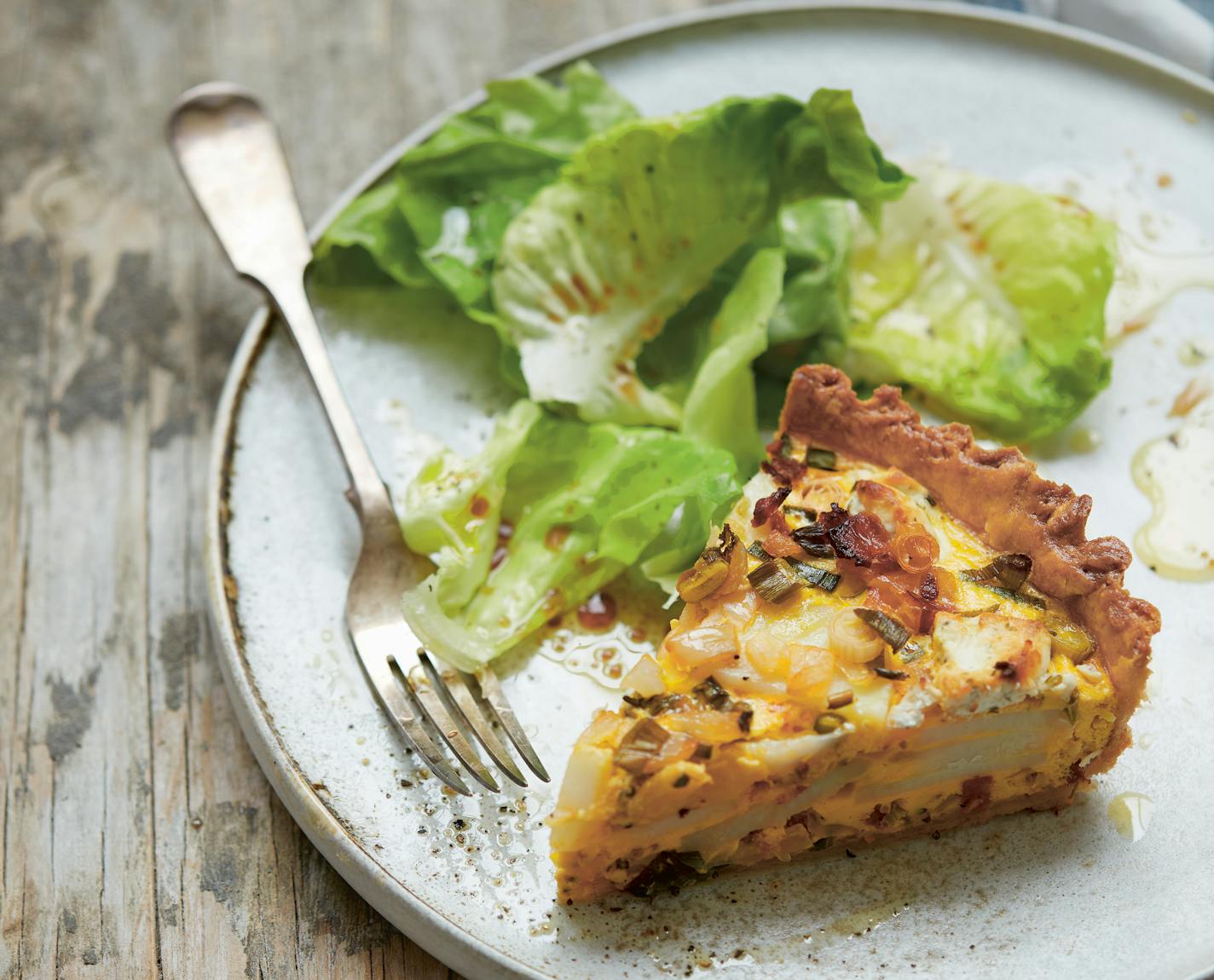 A slice of goat cheese, green onion and potato tart served with salad greens.