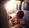 A mother and her baby girl sit in a passenger airline seat. istock