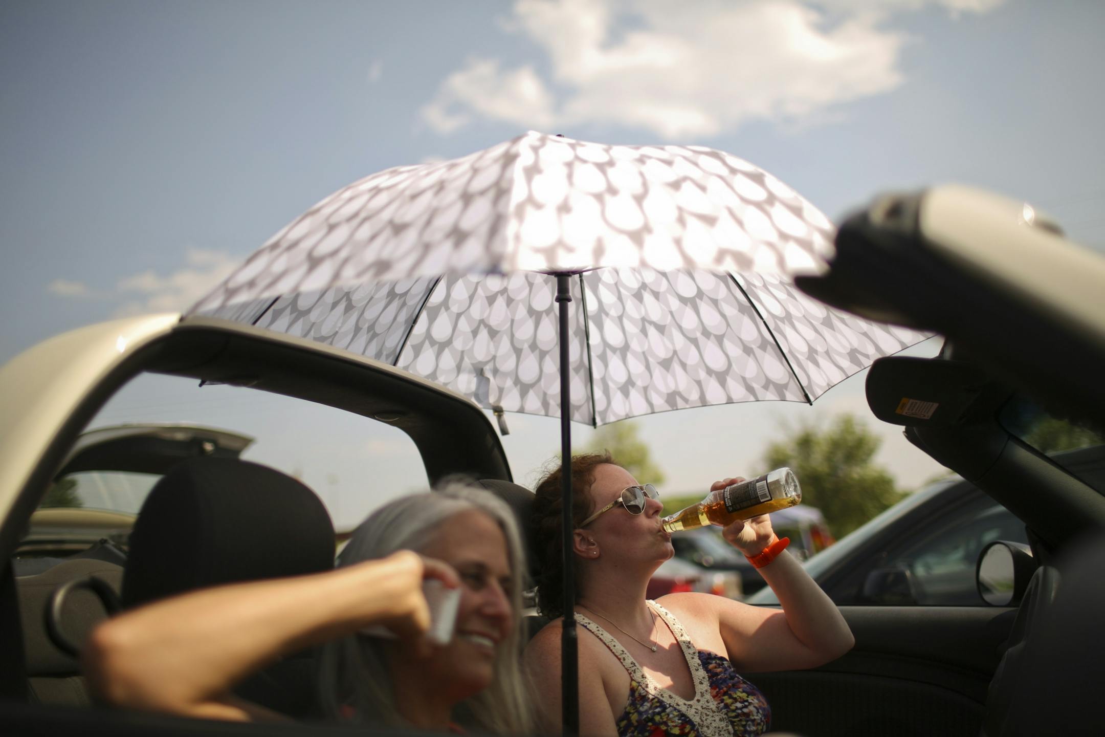Bob Dylan and his Americanarama Festival of Music tour stopped at Midway Stadium in St. Paul, Minn. Wednesday night, July 10, 2013. Many early arrivers tailgated in the parking lot before going in to hear openers Richard Thompson, My Morning Jacket, Wilco, and eventually the night's headliner, the Bard of Hibbing. With the top down on her car and the umbrella up, Heather Mills of Maple Grove took a sip of hard cider while Kristina Schatz of St. Paul coordinated getting the ticket she left at hom