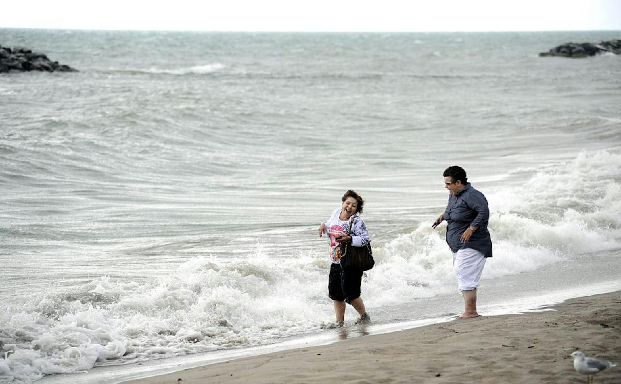 Sisters Angie, left, and Lisa Smith laugh as waves crash at their feet at Beach 7 at Presque Isle State Park in Erie, Pa.
