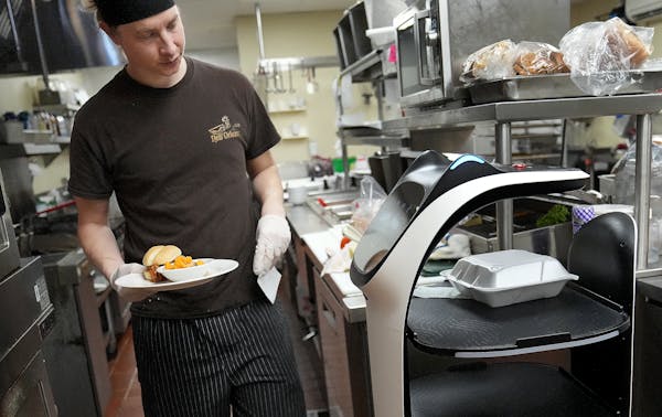 Chef Brennan Danielski loads an order onto a robot, Bella, to bring to the dining room at The Commons on Marice, an assisted-living center in Eagan.