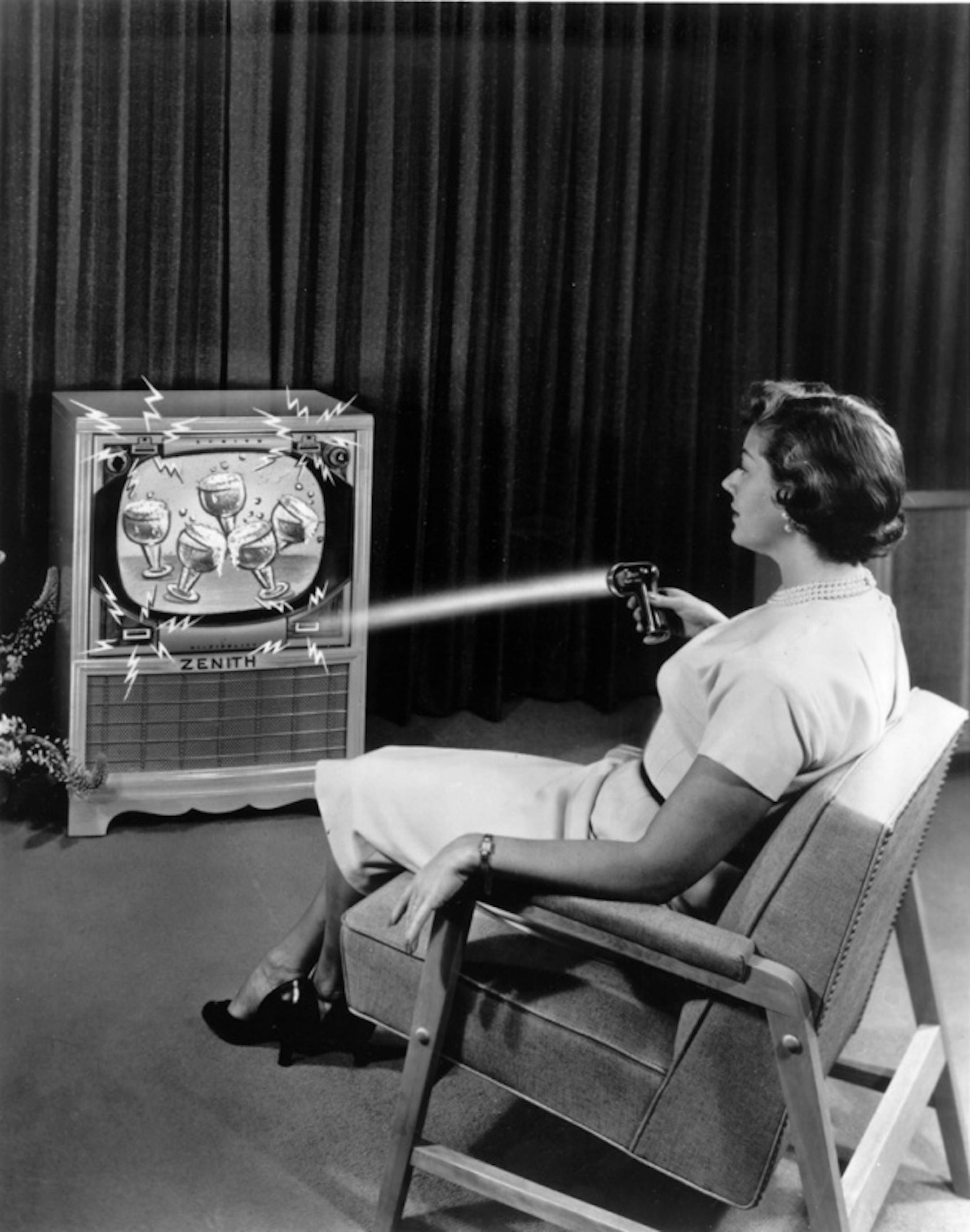 KRT US NEWS STORY SLUGGED: TV-CLICKER KRT PHOTOGRAPH COURTESY OF ZENITH Electronics corp./KRT (KRT13 - July 20 ) This 1955 promotional photograph show's a women using the Flashmatic television remote control from the Zenith Electronic Corp. The flashmatic used a directional flashlight to activate photocells in corners of the TV cabinet. The clicker freed audiences held captive by major networks until the mid-eighties when nearly every new TV included a remote. (KRT) AP PL BL KD (Vert.) (kn) (B&W ONLY) (Additional photo available on KRT Direct,