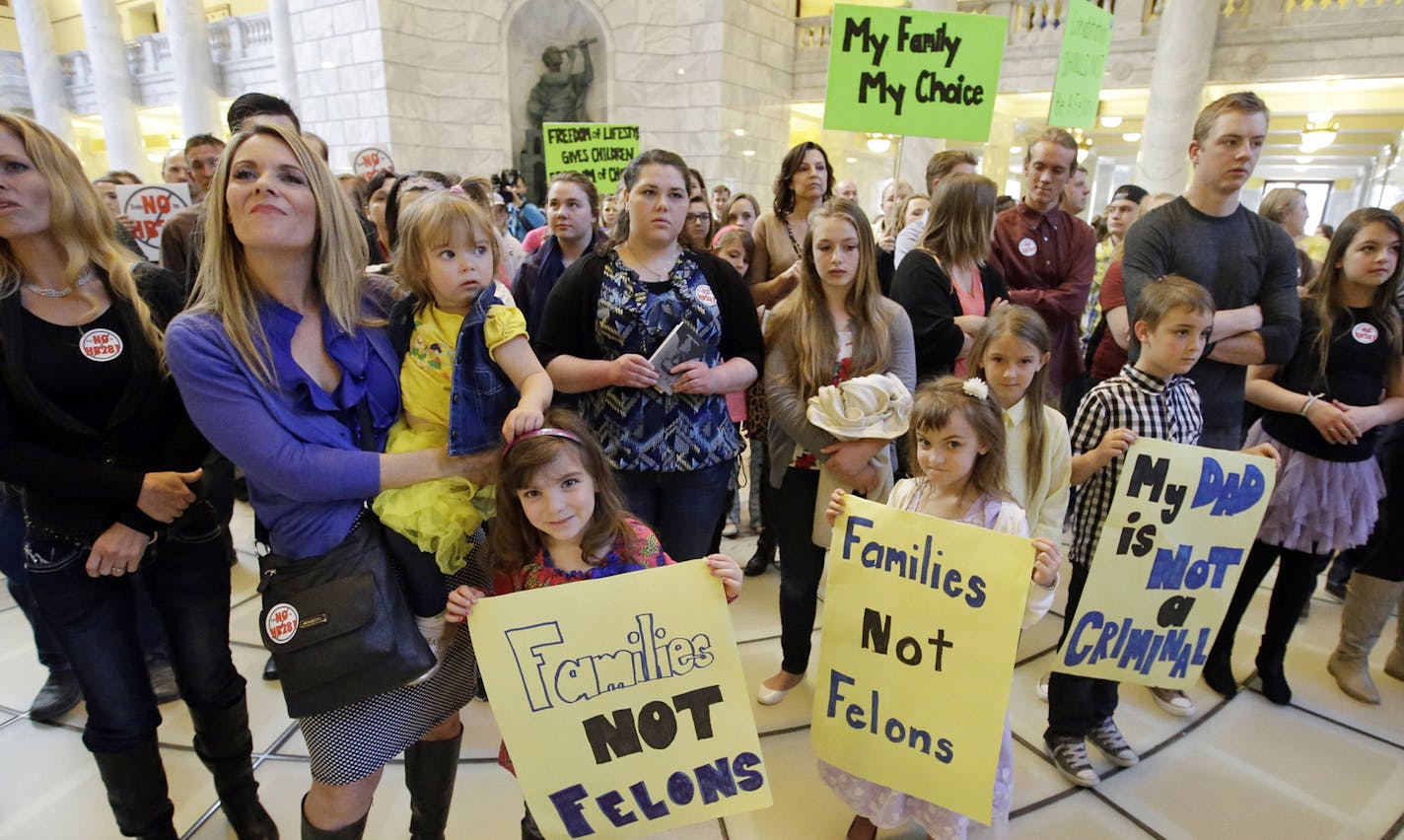 Polygamy advocate Vicki Darger, left, holds her daughter Tess, 2, while her other daughter Tori, 5, center left, holds a sign, as her husband's other wife's daughter Krista, 6, right, also holds a sign during a gathering at the Utah State Capitol to protest a lawmaker's proposal that would make polygamy a felony crime again Monday, March 7, 2016, in Salt Lake City. About 150 pro-polygamy activists and their children protested, holding signs and giving speeches criticizing the proposed law. (AP P