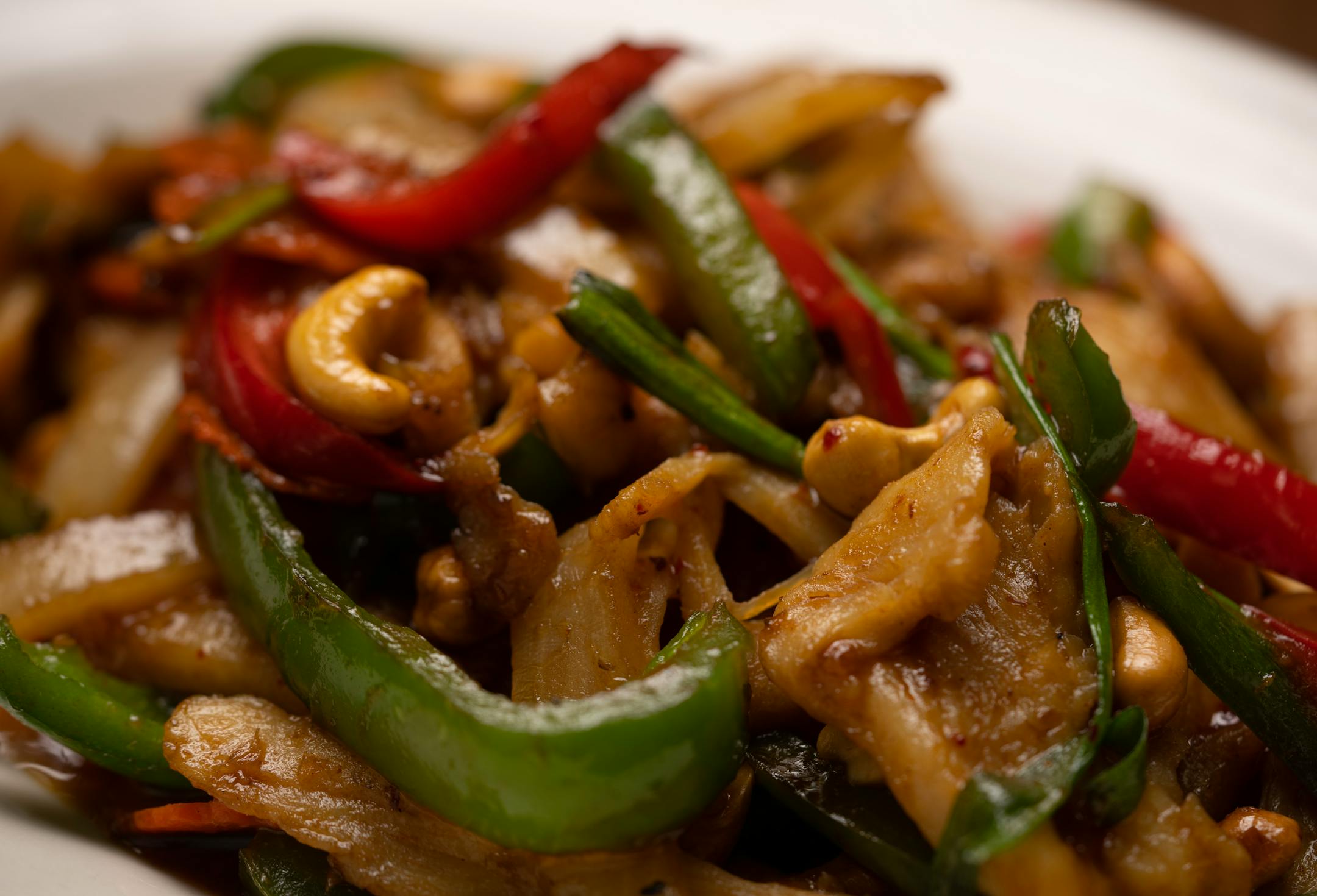 Thai cashew chicken made with boneless chicken, white onions, red and green bell peppers, carrots, cashews, and green onions in a chili paste.