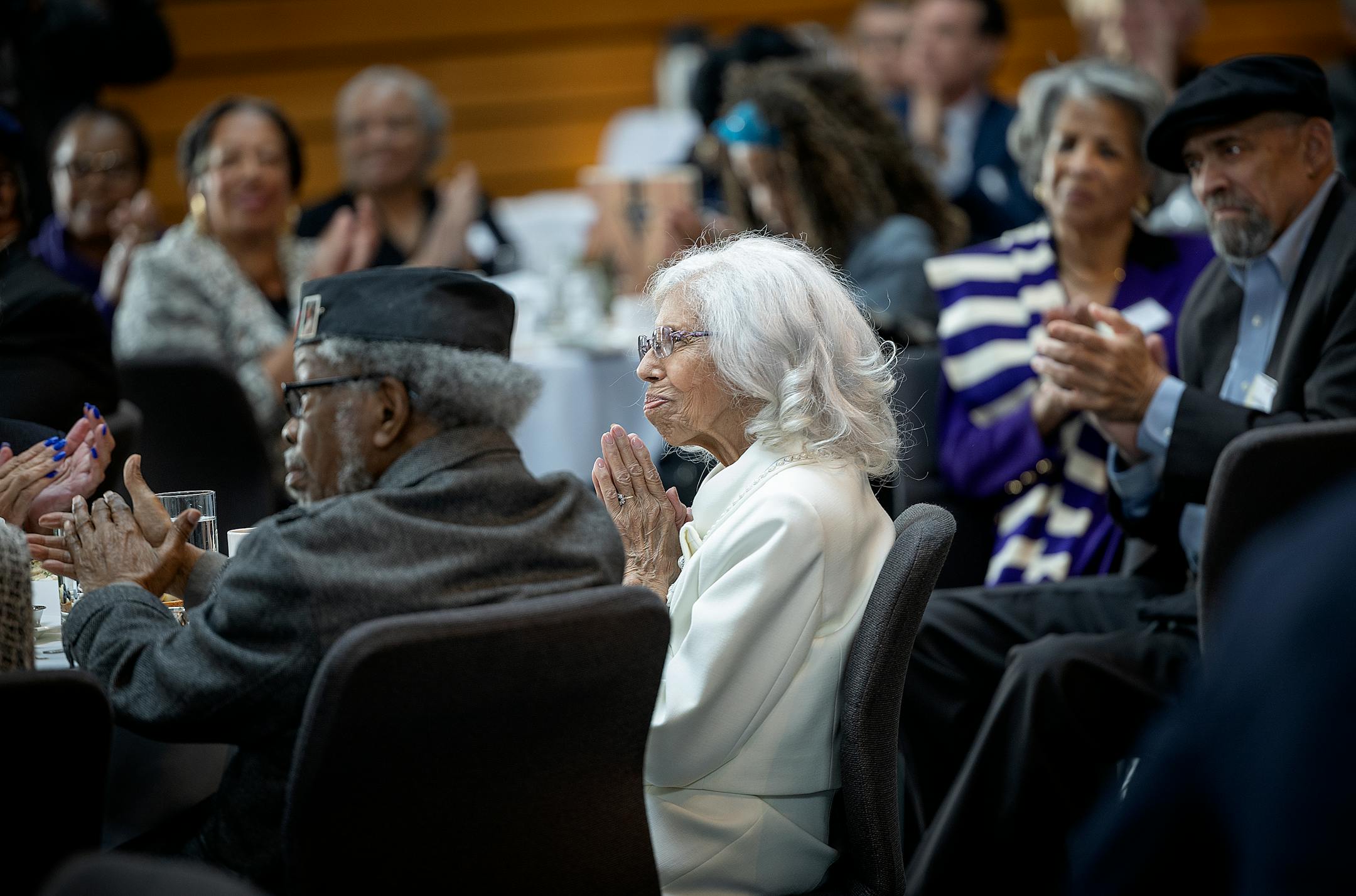 Josie R. Johnson clasps her hands together as dignitaries speak about her at a ceremony.
