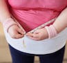 Close-up of overweight woman measuring her waist with tape measure