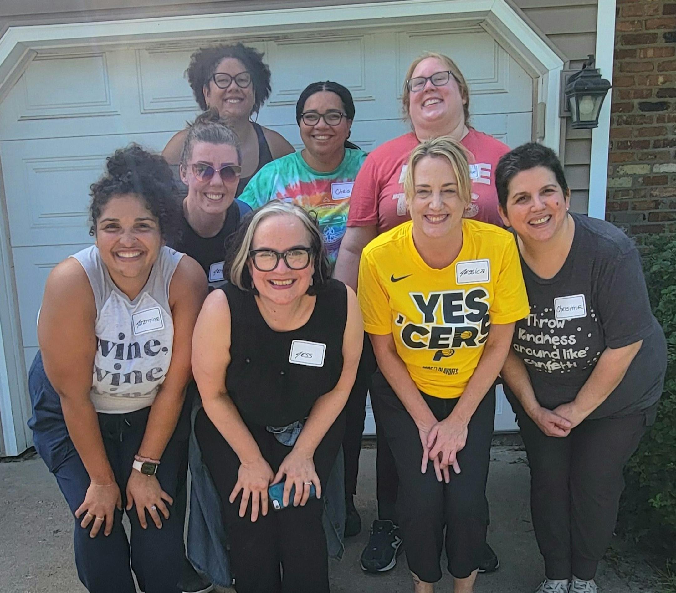 Eight smiling women gather on a suburban driveway to pose for a group picture.
