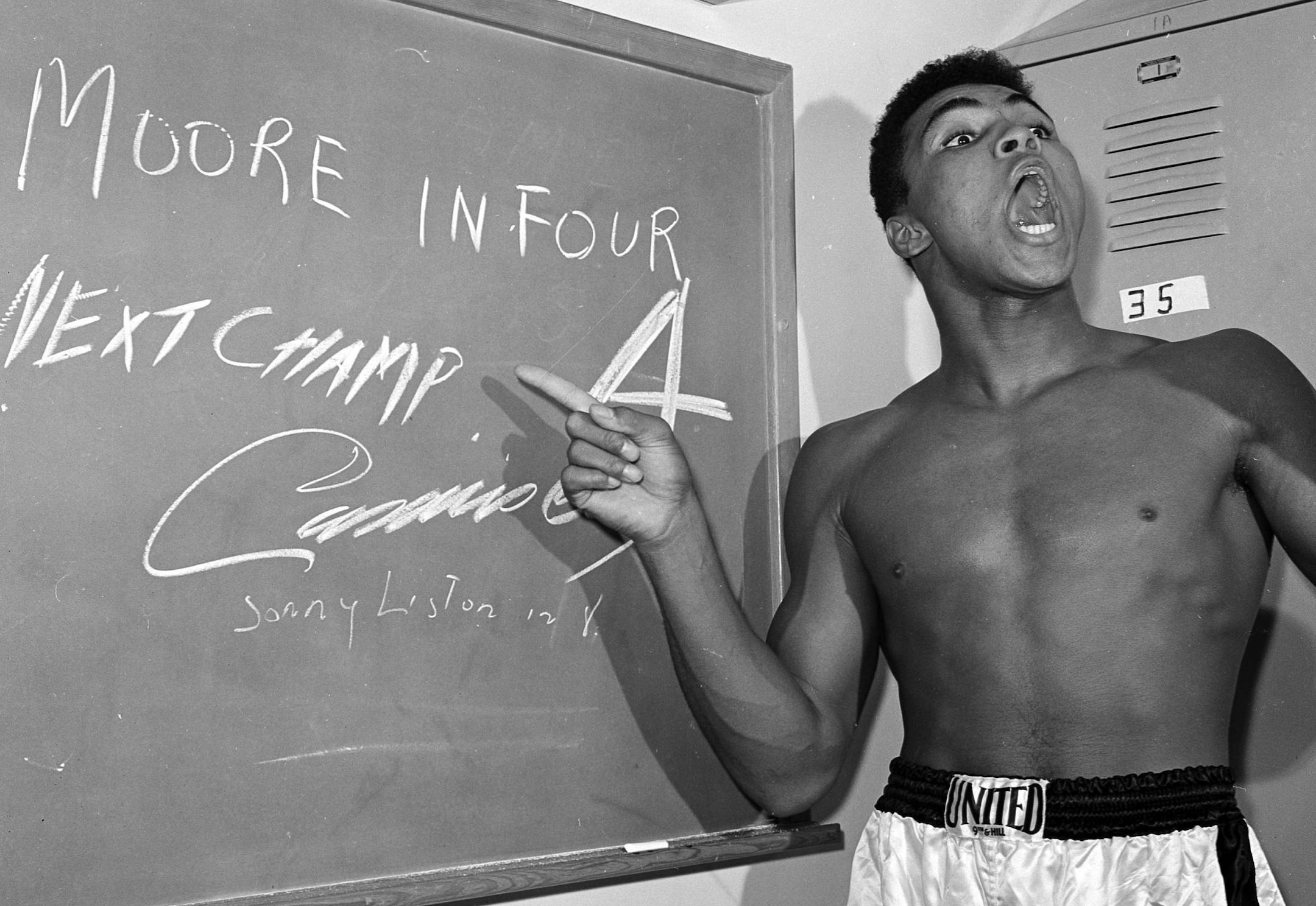 FILE - In this Nov. 15, 1962, file photo, young heavyweight boxer Cassius Clay, who later changed his name to Muhammad Ali, points to a sign he wrote on a chalk board in his dressing room before his fight against Archie Moore in Los Angeles, predicting he'd knock Moore out in the fourth round, which he went on to do. The sign also predicts Clay will be the next champ via a knockout over Sonny Liston in eight rounds. He did it in seven rounds. Ali turns 70 on Jan. 17, 2012.