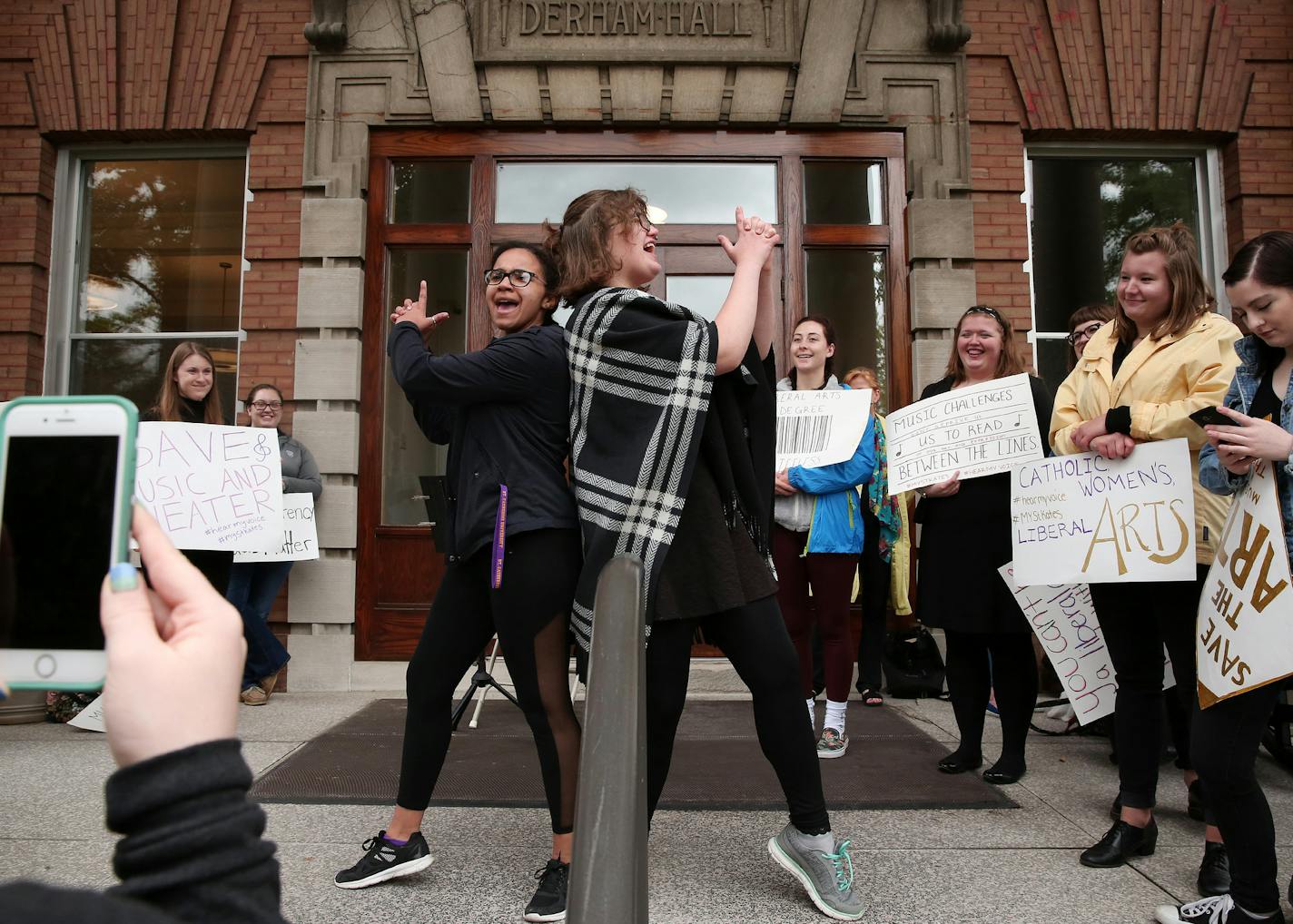 Protesters Maya Butler, left, and Shae Alcamo, both first year students, performed a skit as others held signs and sang songs in front of Derham Hall opposing cuts to the music and theater programs Thursday. ] ANTHONY SOUFFLE &#xef; anthony.souffle@startribune.com Protesters, including choir, soloists, instrumentalists and actors, participated in a protest "sing"-in Thursday, May 18, 2017 in and around Derham Hall opposing cuts to the music and theater programs at St. Catherine University in St.