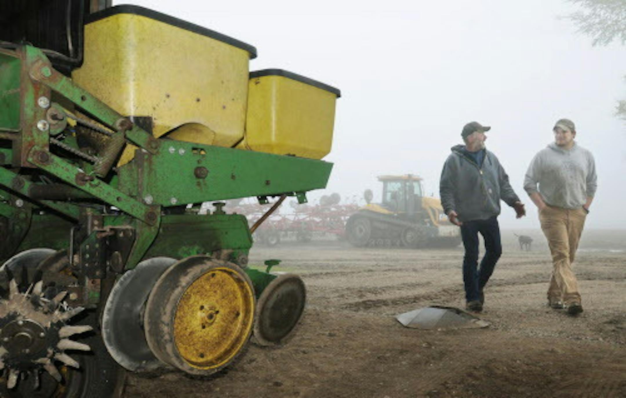 Le Sueur County, Minn. farmer Bob Braun, left, and farming partner Ryan Thelemann walk past a planter idled by wet weather in Le Sueur, Minn., on Tuesday, May 20, 2014. Wet weather has delayed spring planting for many farmers in Minnesota, threatening yields andcrop insurance benefits. (AP Photo/The Mankato Free Press, John Cross)