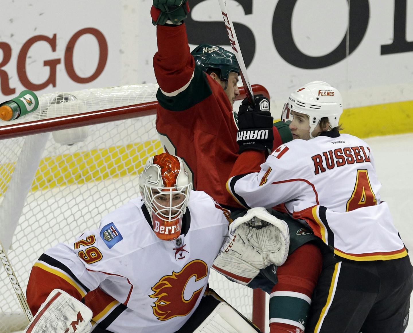 Calgary Flames' Kris Russell, right, shoves Minnesota Wild's Zenon Konopka into the net as Flames goalie Reto Berra, left, defends in the first period of an NHL hockey game, Tuesday, Nov. 5, 2013, in St. Paul, Minn. (AP Photo/Jim Mone)