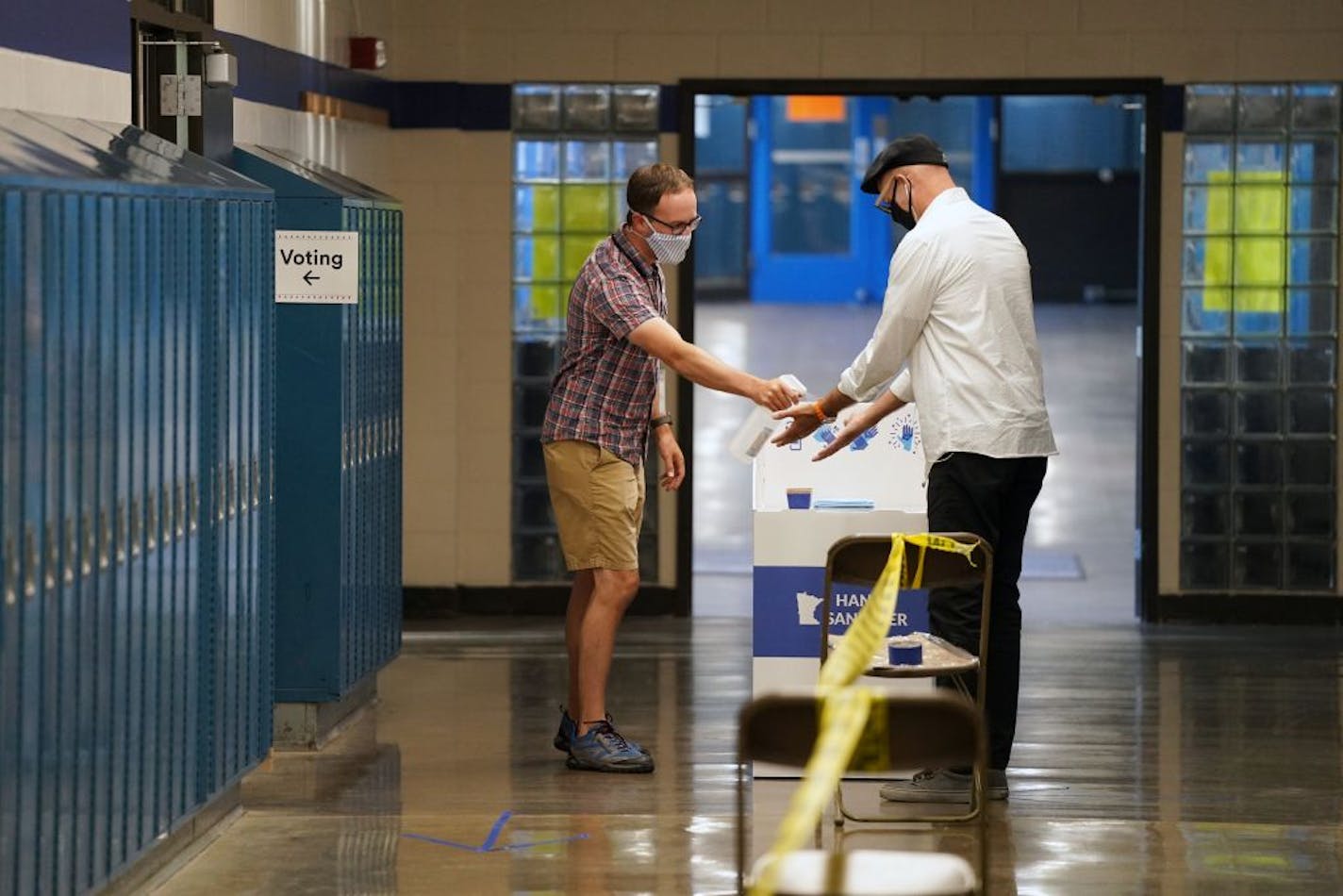 Election judge Tyler Sahnow gave a spray of hand sanitizer to John Enloe as he arrived to vote Tuesday morning at Northeast Middle School in Minneapolis.