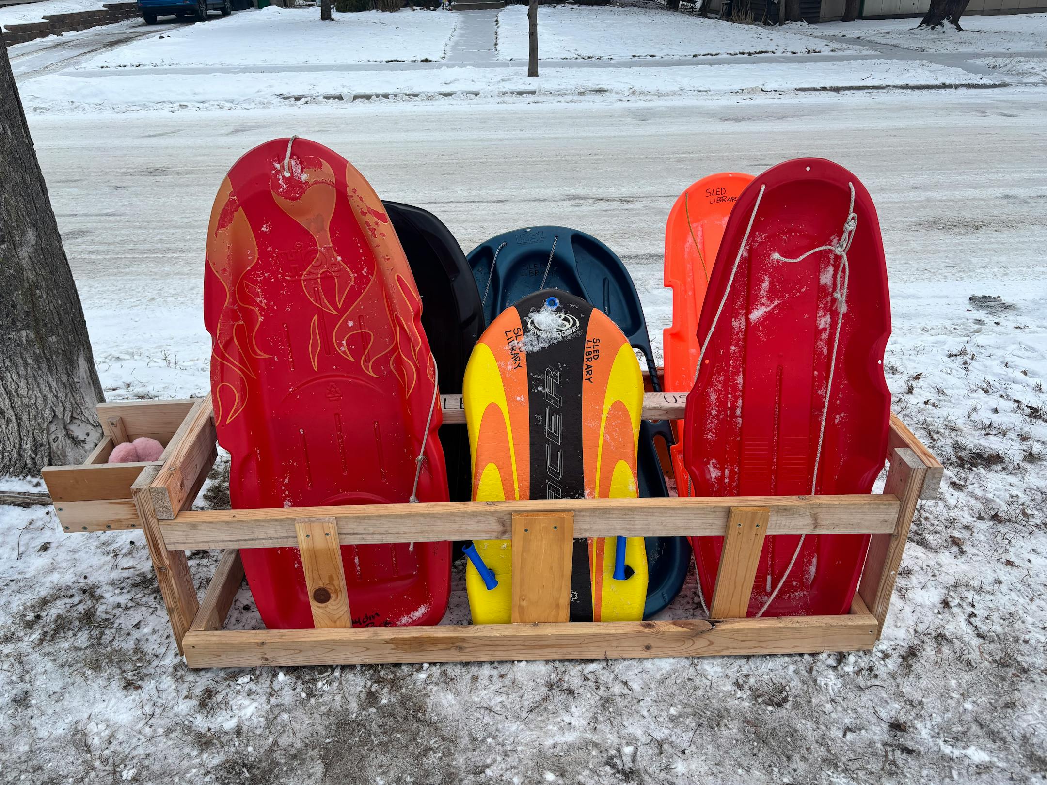 A wood stand holds about a half dozen sleds dusted with snow standing on end.