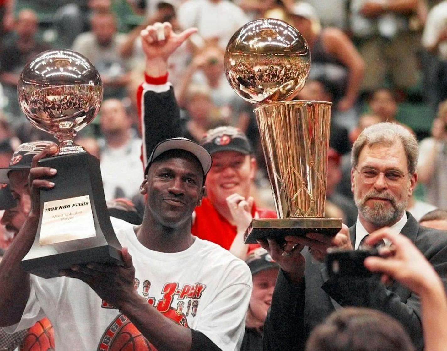 Michael Jordan holds the MVP trophy while coach Phil Jackson holds up the championship trophy after the Chicago Bulls won the 1997-98 NBA title.