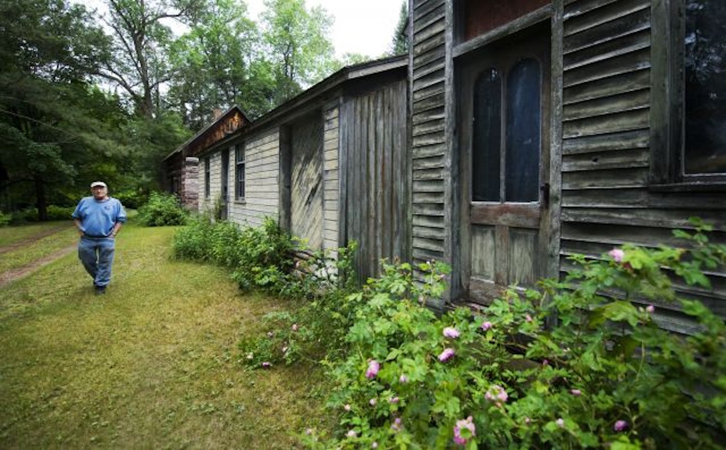 Ron Wienhold walks down the path through his property past his log cabin, historic drugstore, and other shop.