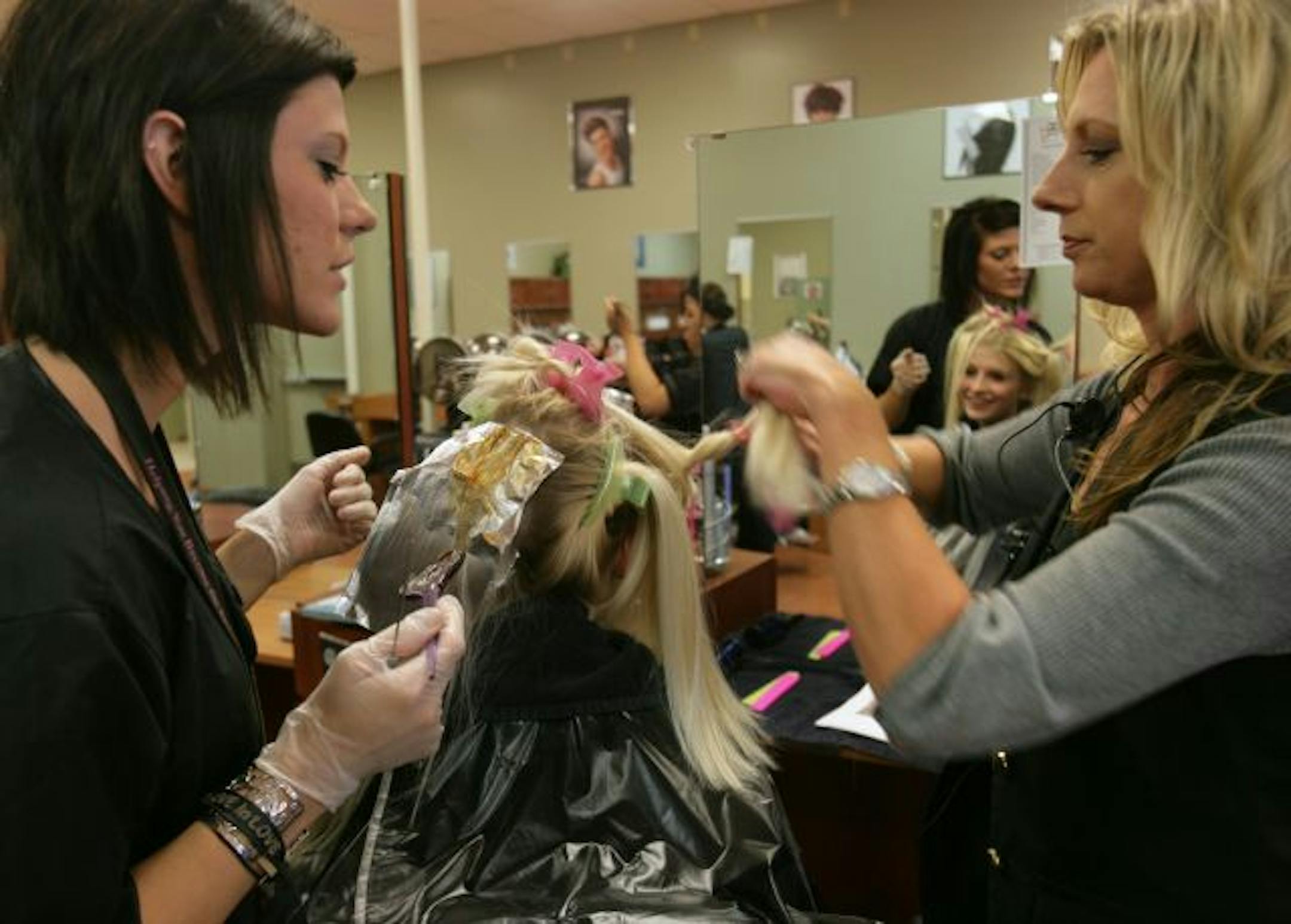 Student Kellie Meier (left) watches as instructor Angela Ericson shows her a full head foil with highlights and lowlights technique on client Kensia Harrison at Minnesota School of Beauty in Lakeville, Minnesota.