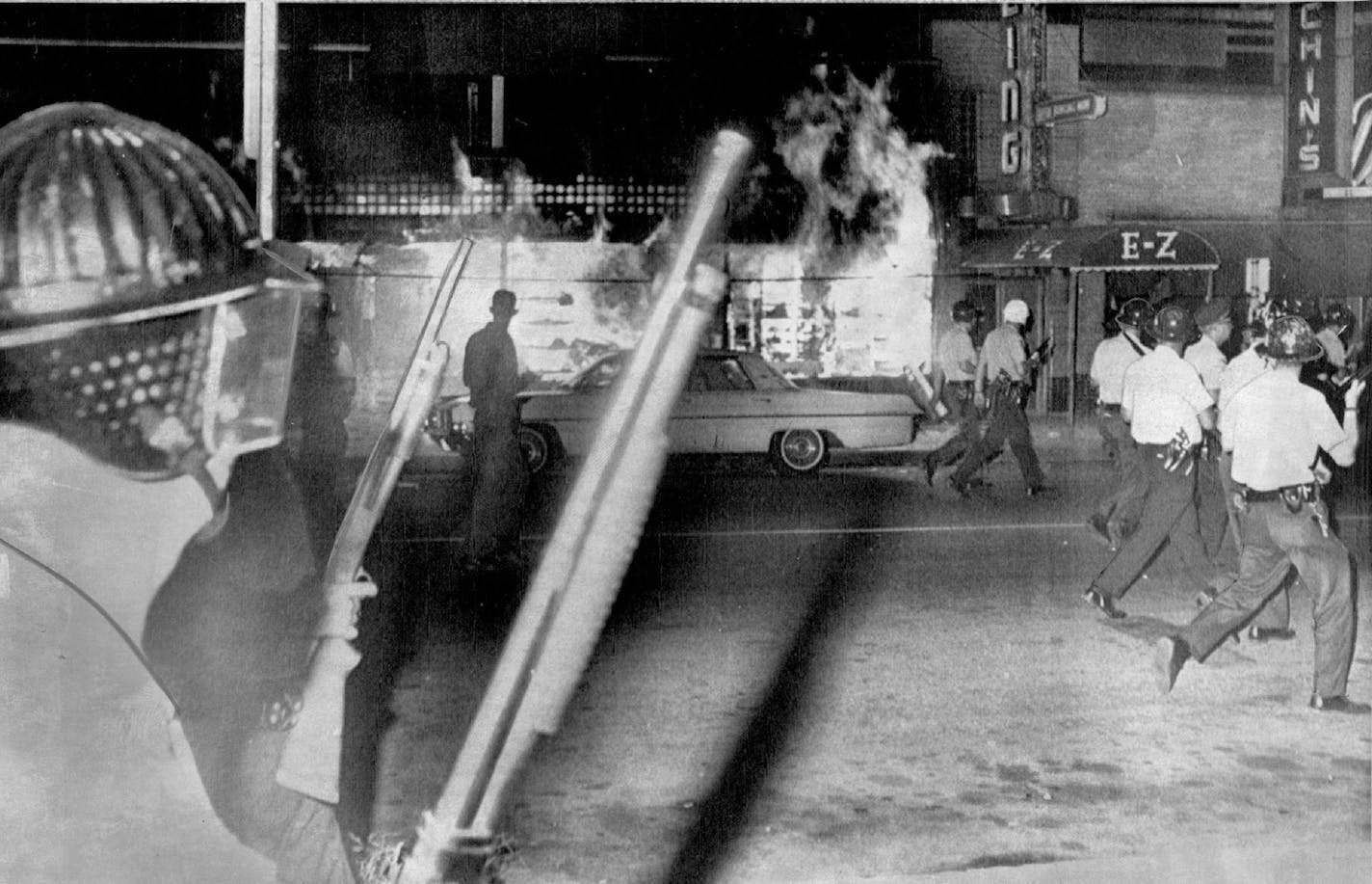 July 21, 1967 Police Clear Street-Helmeted Minneapolis police, armed with shotguns, pass blazing grocery store on Plymouth Ave. in north Minneapolis late Thursday night as they begin to clear crowd of unruly negro youths in a second night of violence in this predominantly negro area. Fire bombs were thrown and minor looting was reported. The police marched shoulder to-shoulder down a three block long section to clear path for firefighters and halt looting. RW, AP Wirephoto ORG XMIT: MIN201406241