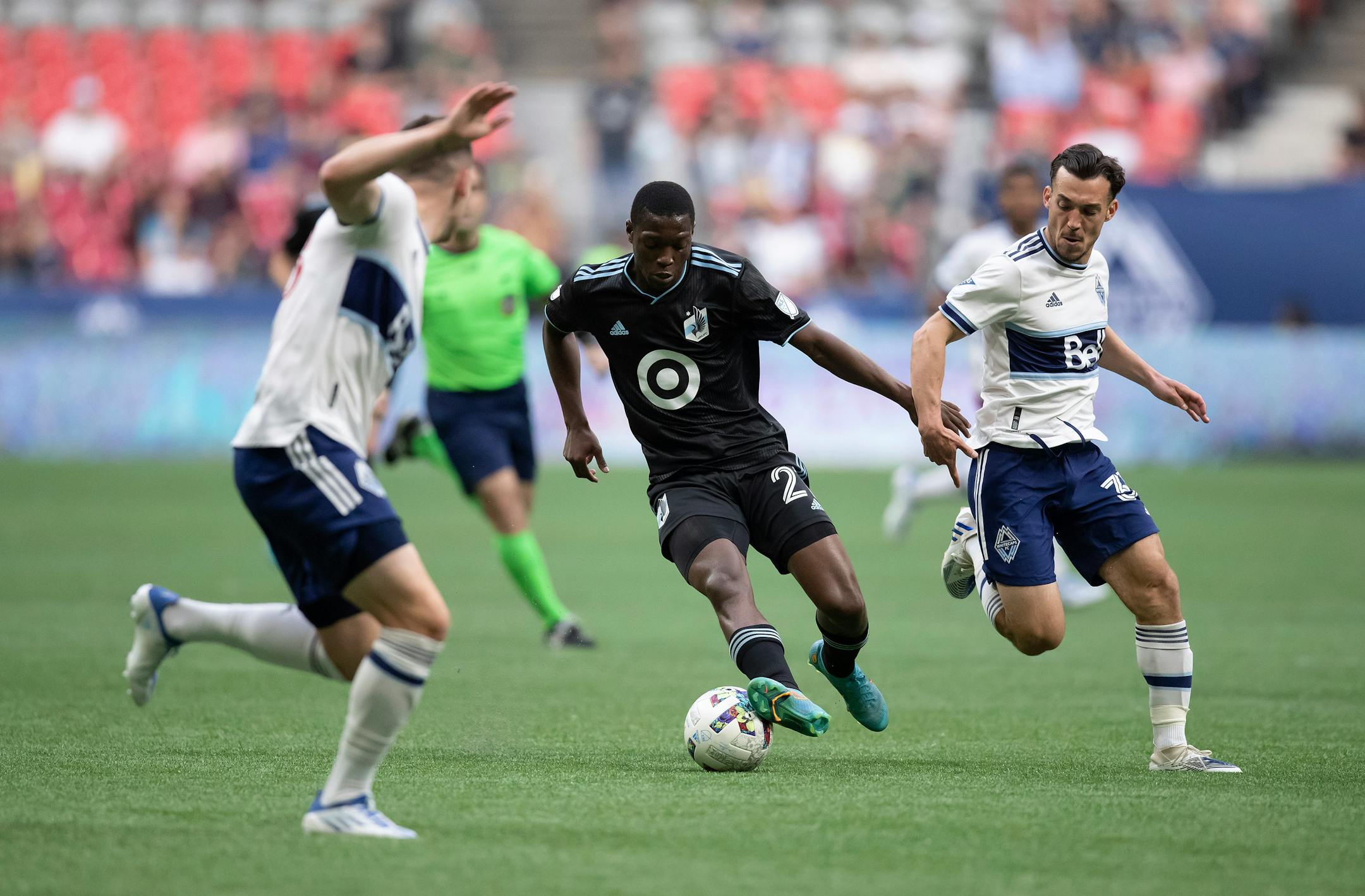 Minnesota United's DJ Taylor, center, moves the ball past Vancouver Whitecaps' Russell Teibert, right, during the first half of an MLS soccer match Friday, July 8, 2022, in Vancouver, British Columbia. (Darryl Dyck/The Canadian Press via AP)