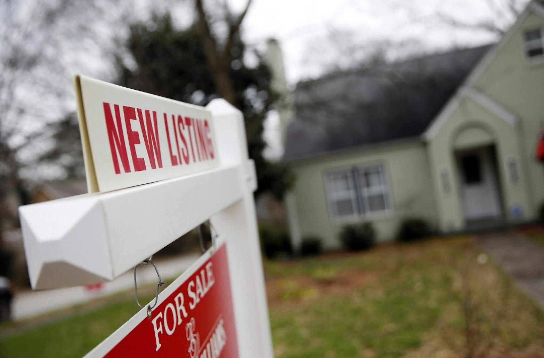 A "For Sale" sign hangs in front of an existing home.