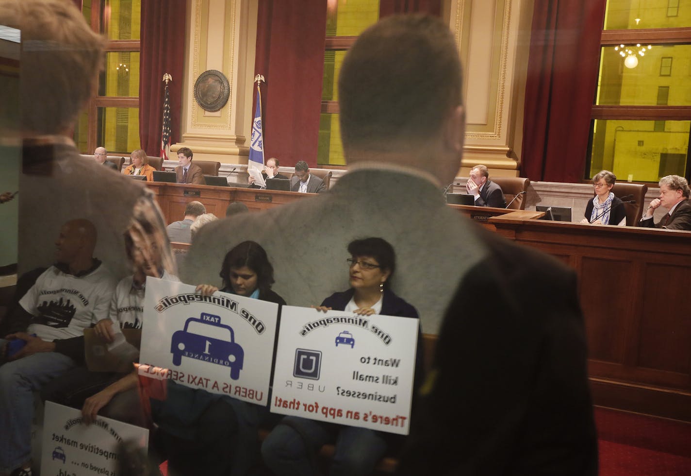 Bambi Barclay ,right, and fellow drivers for Blue & White Taxi were reflected in the glass of a door at Minneapolis City Hall during the hearing on Tuesday.