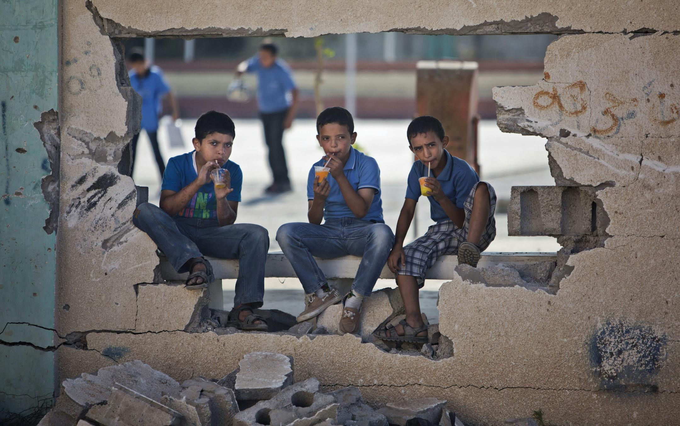 Palestinian school boys drink iced juice as they sit on a damaged wall of a school in Gaza City's Shijaiyah neighborhood, Sunday, Sept. 14, 2014. Some half million Gaza children made a delayed return to school on Sunday after a devastating 50-day war with Israel that killed more than 2,100 Palestinians and damaged hundreds of school buildings. (AP Photo/Khalil Hamra)