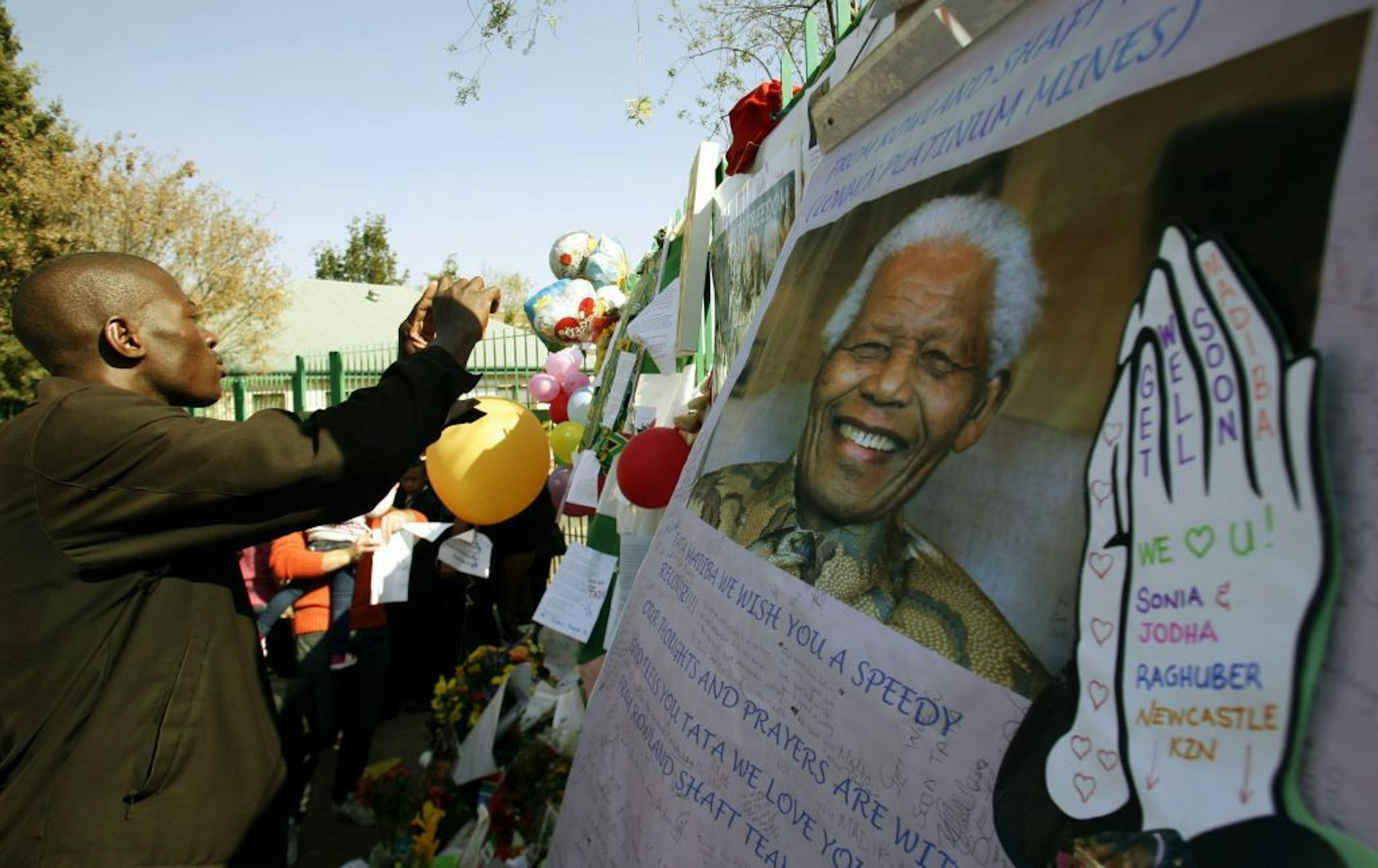 Unidentified man takes a photograph of picture former South African President Nelson Mandela and well-wishers message outside the Mediclinic Heart Hospital where is being treated in Pretoria, South Africa Sunday, June 30, 2013. South Africans in Sunday services have been praying for former President Nelson Mandela who is spending his 23rd day in a Pretoria hospital in critical condition.