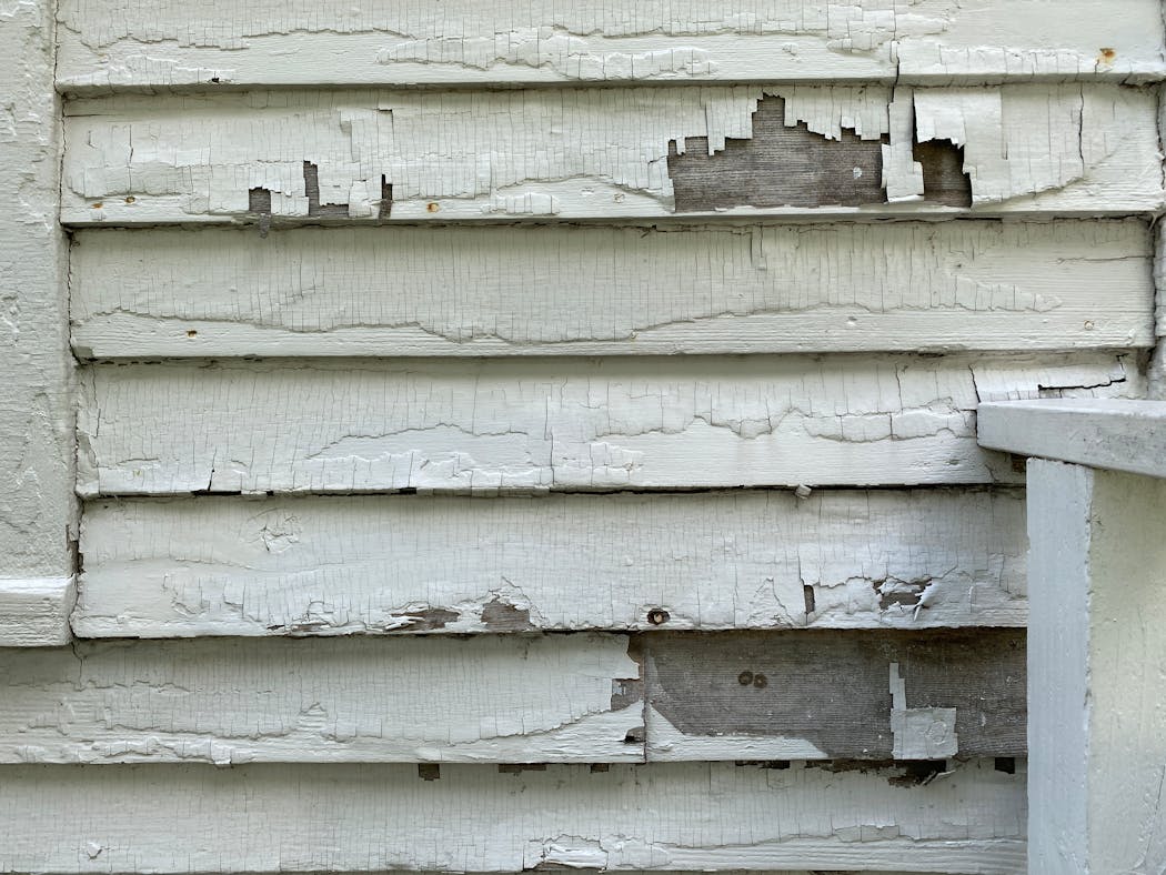 The wood siding of the Stevens House is visible beneath cracking and peeling paint beside the front door of the landmark.