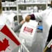 In this file image, Canadian and American flags sit in the foreground as Canadian pharmacist Amanda Hutchinson, left, hands fellow pharmacist Florence