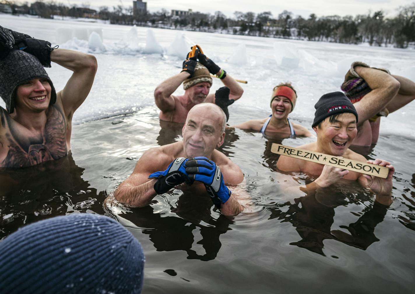 From left, Dane Edward Miller, Leo Royzman and Chad Juncker (with sign) embrace the ice bath hack. Throughout the winter, biohackers maintain a hole in the ice on Cedar Lake in the belief that regular cold-water immersions make them healthier.