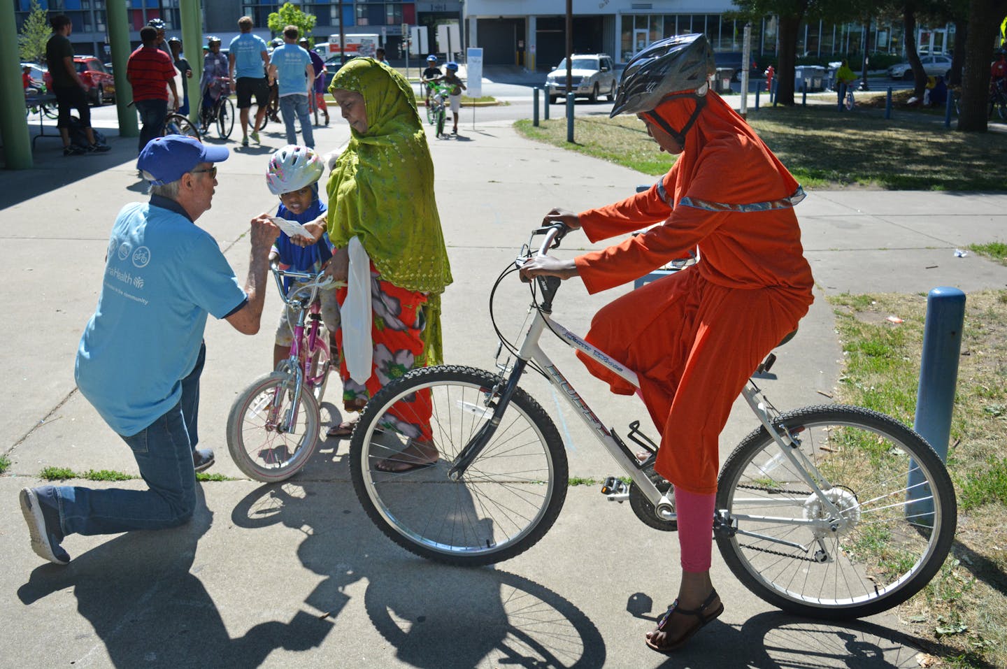 Ken New, a Volunteer of Allina Health telling road safety measures to a kids and his mother outside Brian Coyle Community Center. Photo credit: Salman Yousafzai/Star Tribune