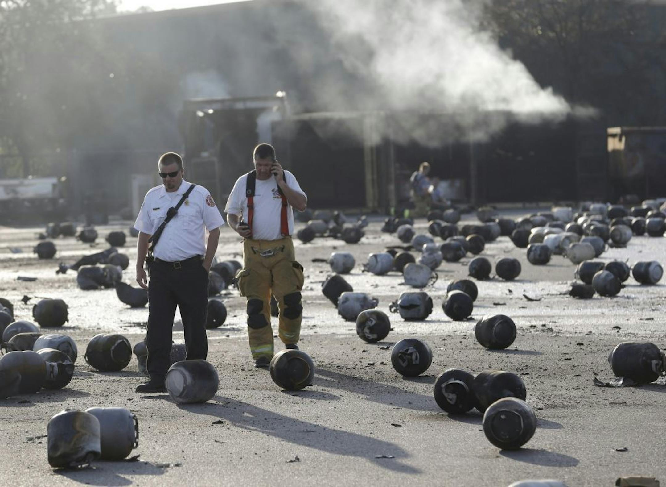 Firefighters walk through an area of exploded propane cylinders in the aftermath of an explosion and fire at a propane gas company, Tuesday, July 30, 2013, in Tavares, Fla. Eight people were injured, with at least three in critical condition. John Herrell of the Lake County Sheriff's Office said early Tuesday there were no fatalities despite massive blasts that ripped through the Blue Rhino propane plant late Monday night.