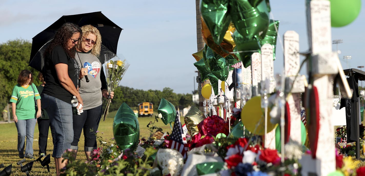 Andrea Clements, left, and Cindy Cappadona pause before placing flowers at the memorial for the victims of the Santa Fe High School shooting Wednesday, May 23, 2018 in Santa Fe, Texas. The two women, both from Santa Fe, were there to show their support to the teachers who returned to work today. (Jennifer Reynolds/The Galveston County Daily News via AP)