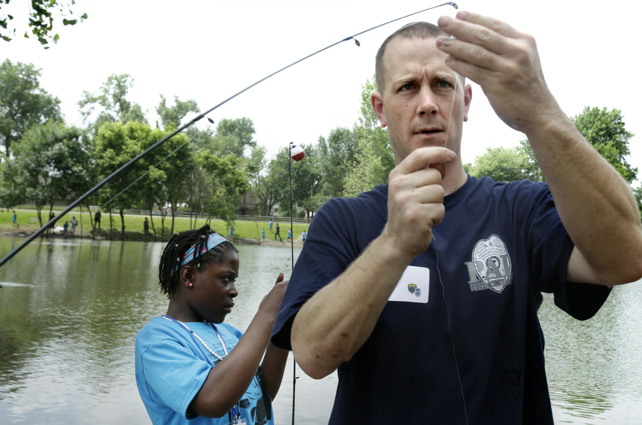 Patrol officer Jarod Miller helped untangle a fishing line as Destiny Freeman worked on baiting her hook at the Brooklyn Park Community Center. Brooklyn Park, MN. June 26, 2013. ] JOELKOYAMA‚Ä¢joel koyama@startribune.com On Wednesday, June 26th at a pond outside the Community Center on 85th Ave., police officers will take 150 of the city neediest kids fishing. It's all part of an effort to show at-risk children between the ages of 7 and 12 that police officers not only protect a