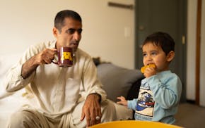 Abdul Saboor Qaderi sips coffee as his youngest son, Elham, 2, eats a cookie in their new home in St. Paul on May 22, two months after arriving from a
