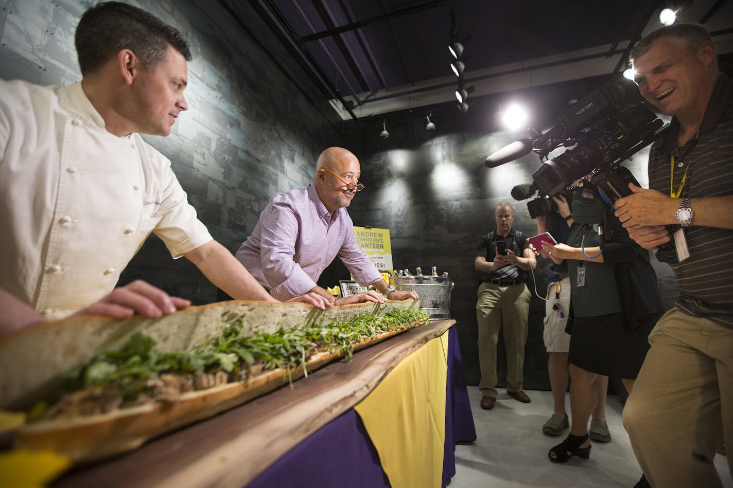 Chefs Gavin Kaysen, left, and Andrew Zimmern, center, show off a giant Italian roast pork sandwich to the media while debuting their new concept AZC Hoagies which will feature sandwiches at U.S. Bank Stadium. ] (Leila Navidi/Star Tribune) leila.navidi@startribune.com BACKGROUND INFORMATION: Officials with the Minnesota Vikings, the Minnesota Sports Facilities Authority and Aramark announce some of the local culinary partners that will be featured at U.S. Bank Stadium during a press conference on