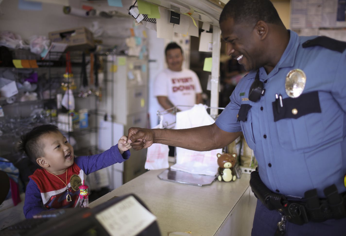 Officer Denson fist-bumped Jaden Vang after giving him a sticker in his dad&#x2019;s market (Cha Vang, rear) on Rice Street on Wednesday.