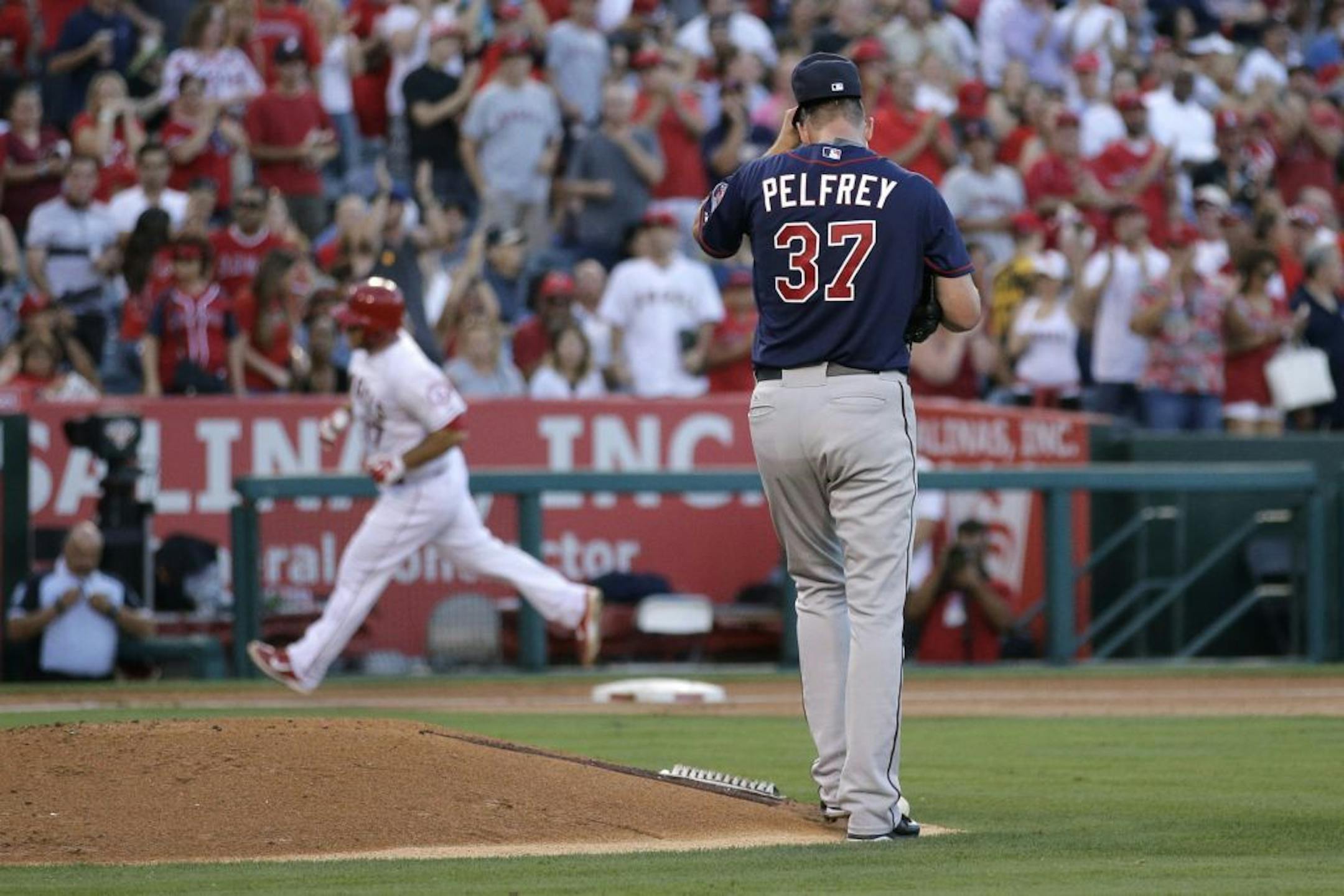 Minnesota Twins starting pitcher Mike Pelfrey adjusts his cap as Los Angeles Angels' Chris Iannetta, background, rounds the bases on a home run during the second inning of a baseball game, Wednesday, July 22, 2015, in Anaheim, Calif.