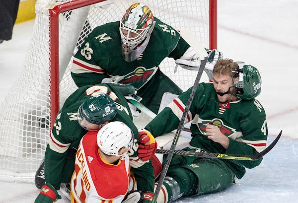 Mikael Backlund of the Flames gets tangled up with Cam Talbot, Connor Dewar (52) and Jon Merrill (4) of the Wild in the third period