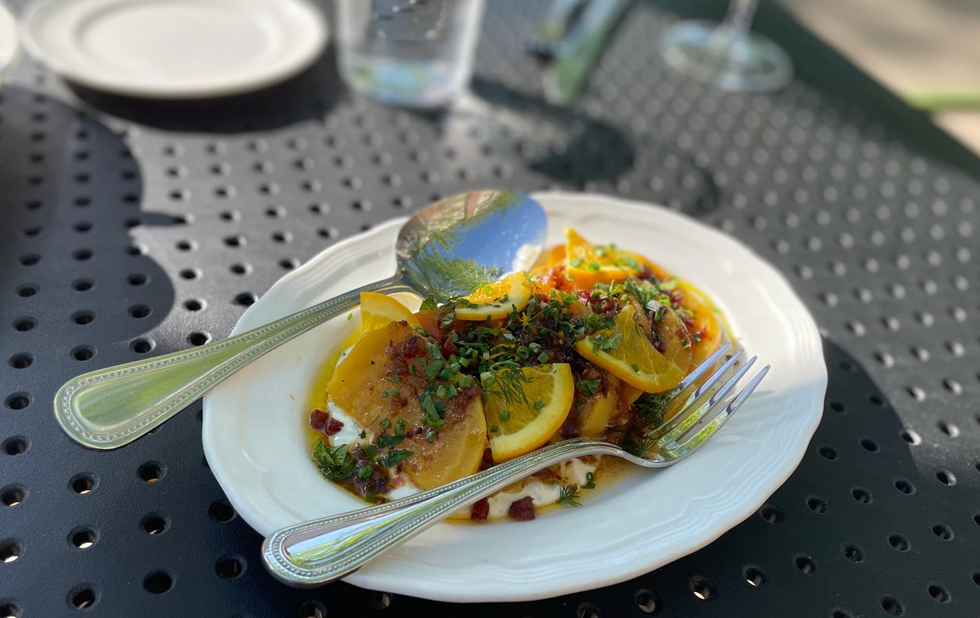A white plate is layered with a creamy sauce, slices of golden beets that almost look like stained glass in the afternoon sunlight, topped with thin wedges of oranges and crumbles of sausage.